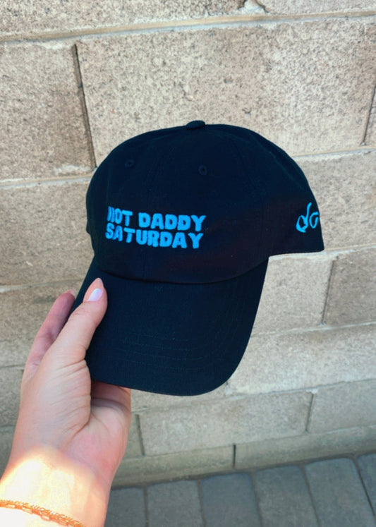 Black cap with blue text held by a hand against a stone wall background
